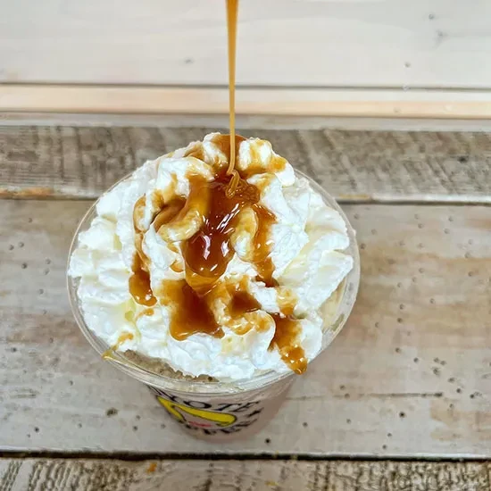 Caramel sauce drizzling over whipped cream in a clear plastic cup.