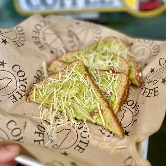 Avocado toast slices with cheese on branded Coyote Coffee paper.