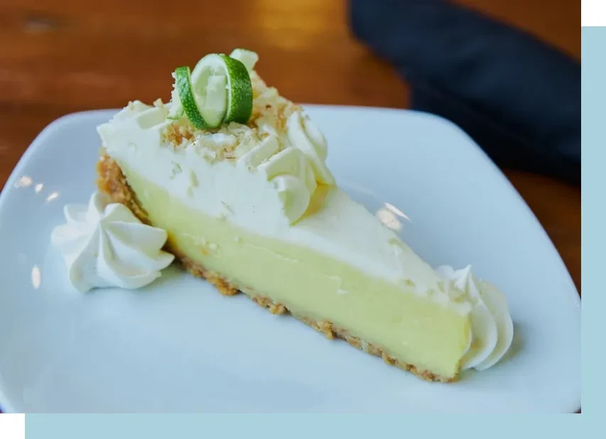 Key Lime Pie slice topped with whipped cream and lime peel.