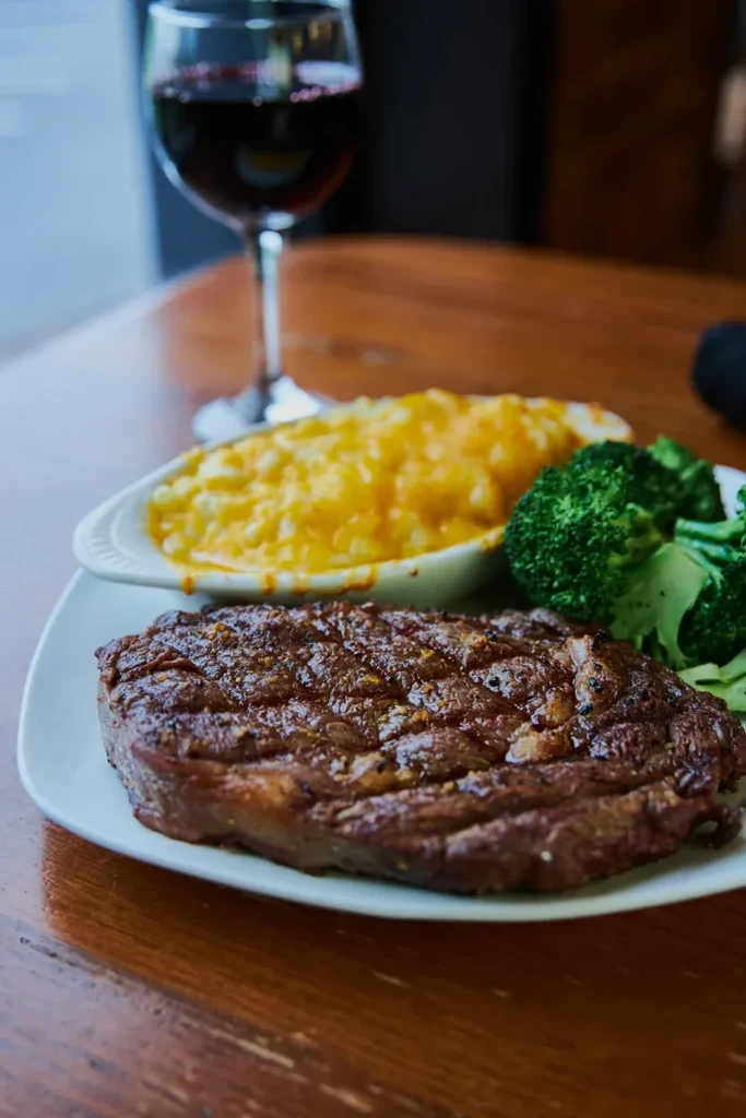 Grilled steak, broccoli, and macaroni and cheese on a wooden table.