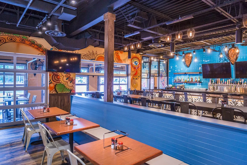 Modern, empty restaurant interior showing colorful murals, seating, and a bar.