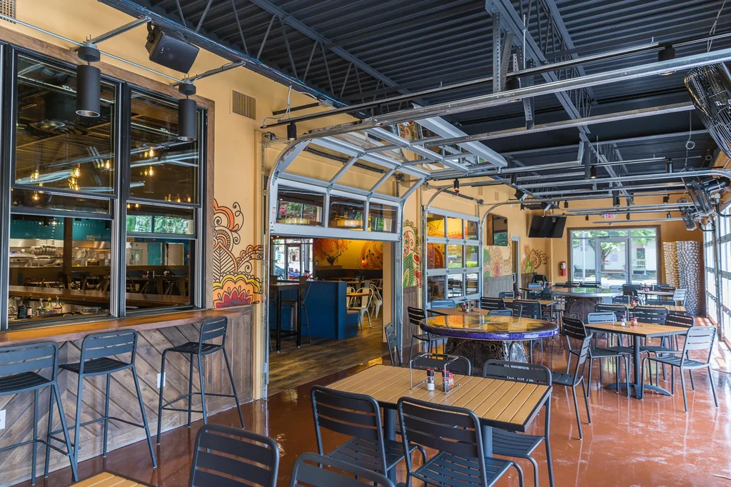 Modern industrial restaurant interior with varied seating and open glass doors.