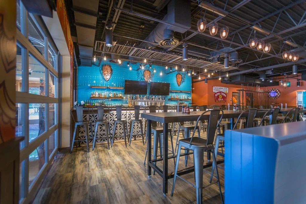 Empty modern restaurant bar with turquoise tiled wall and industrial ceiling.