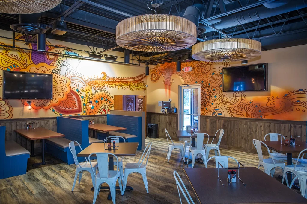 Vibrant mural, industrial ceiling, and blue booths in an empty modern restaurant.