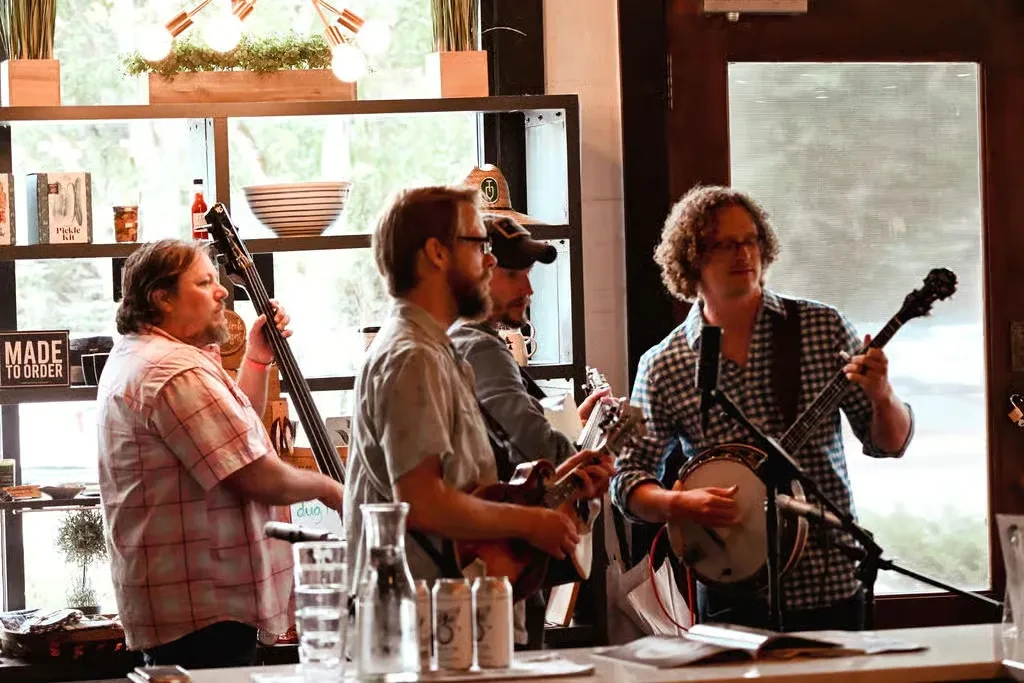 Four male musicians play bass, mandolin, guitar, and banjo live.