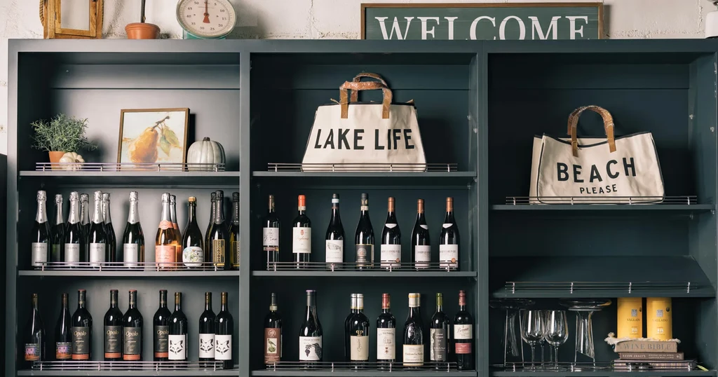 Teal shelving unit neatly organized with wine, books, decor, and tote bags.
