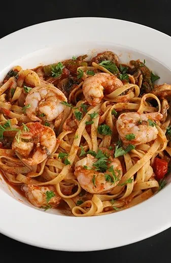Fettuccine pasta with shrimp in reddish-orange sauce, garnished with herbs.