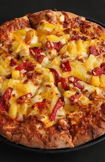 Whole pizza with pineapple, red peppers, and melted cheese.