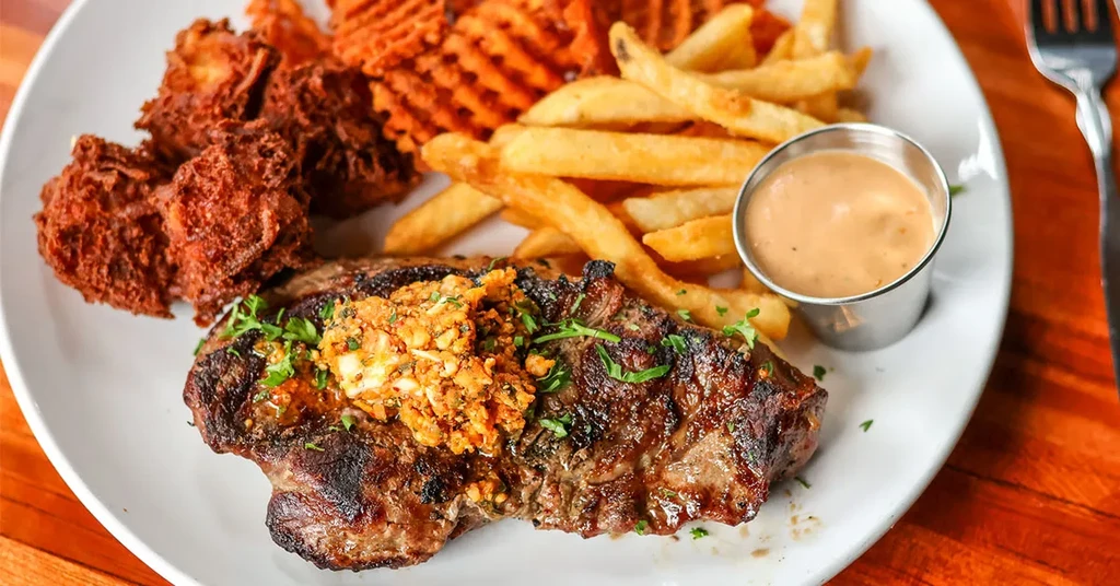 Overhead: Grilled steak with herb butter, two fries, fritters, and sauce.