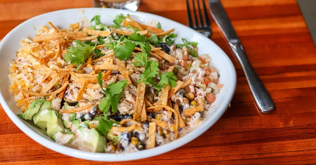 A colorful chicken and rice bowl with avocado, salsa, and tortilla strips.