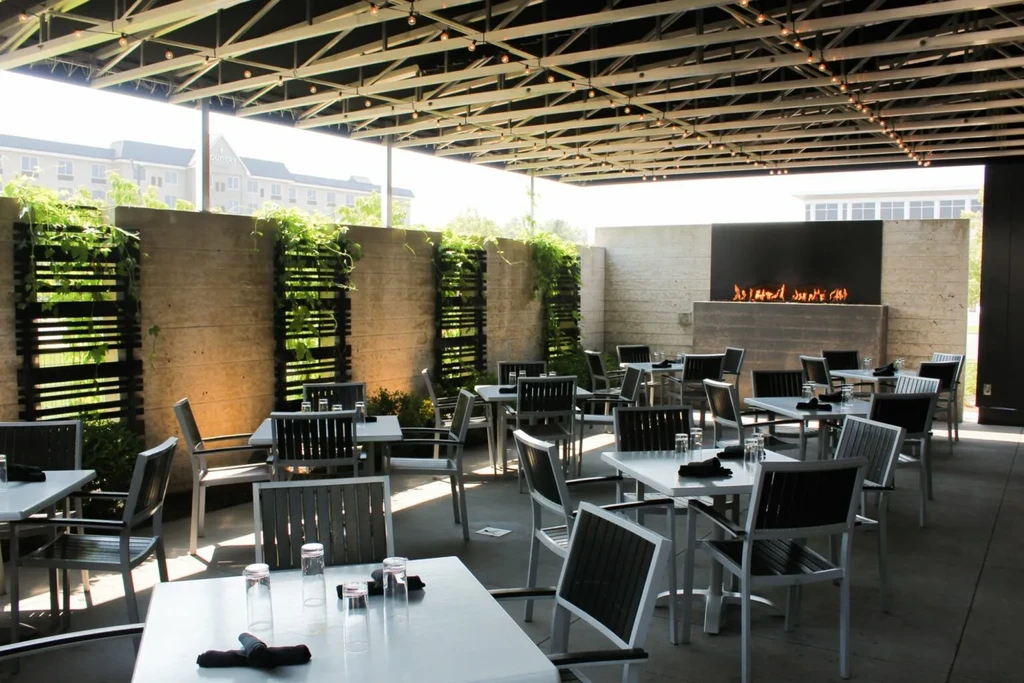 Empty, modern restaurant patio with trellis, green vines, and fireplace.