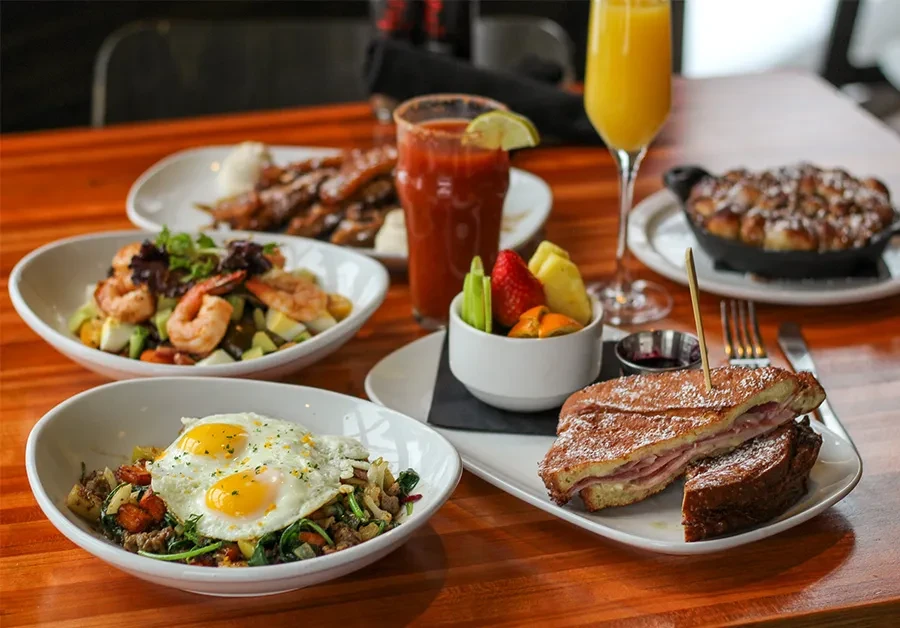 Brunch spread: fried eggs, sandwich, Bloody Mary, Mimosa, pastry.