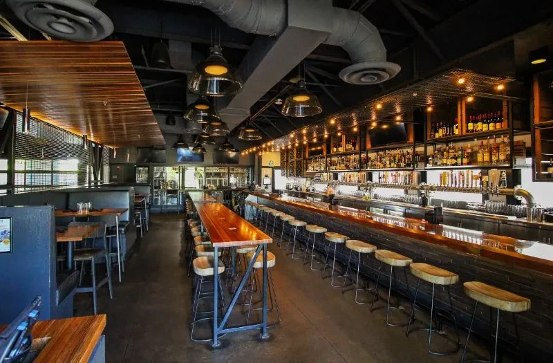 Empty industrial restaurant interior showing bar, booths, and high-top table.