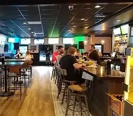 Lively modern restaurant and bar interior with patrons and TVs.