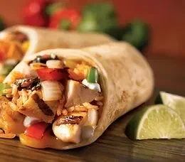 Burrito cut in half, revealing filling, served with lime on wood.