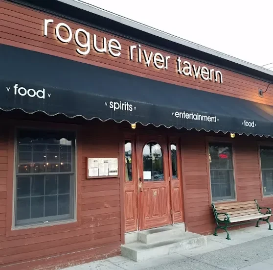 Rogue River Tavern building exterior, reddish wood, dark awning, arched doors.