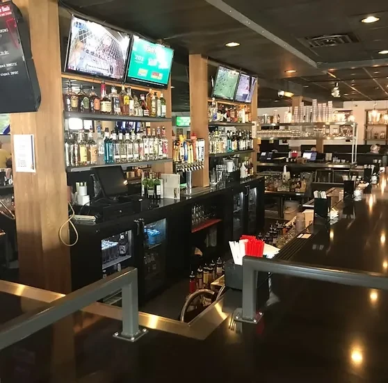 A modern bar counter stocked with liquor, beer taps, and televisions.