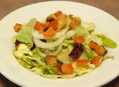Creamy salad with lettuce, tomato, onion, croutons on a white plate.