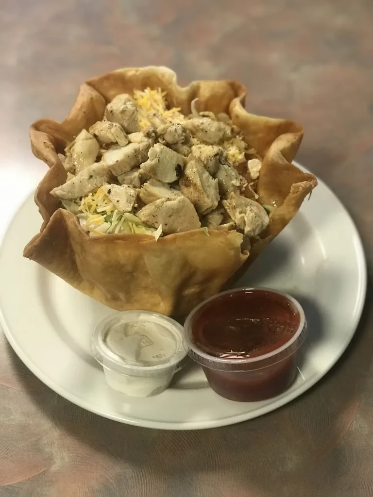 Fried tortilla bowl filled with chicken, lettuce, cheese, and two sauces.