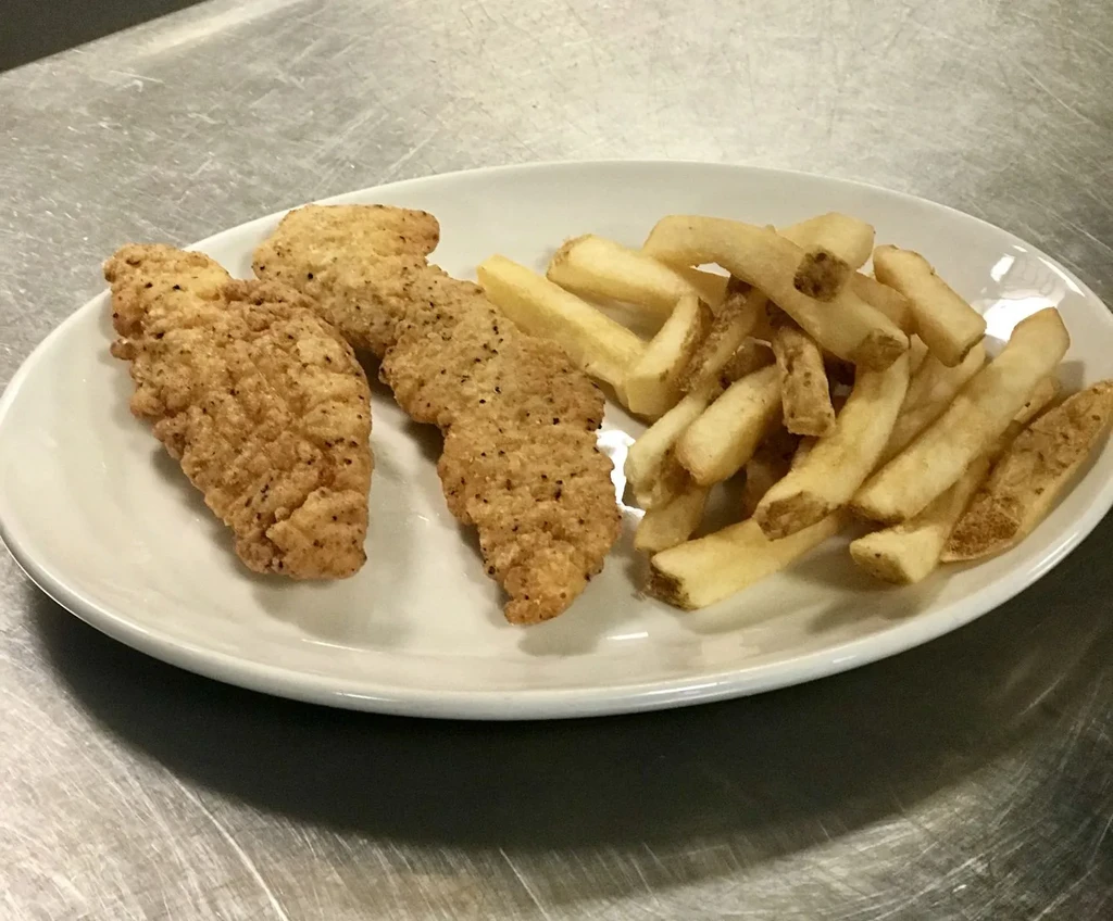 White plate of chicken tenders and fries on metallic surface.