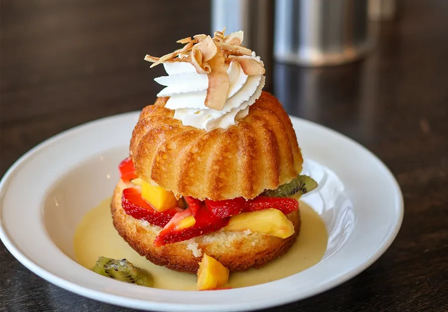 Golden-brown bundt cake, fruit-filled, with cream, coconut, and yellow sauce.