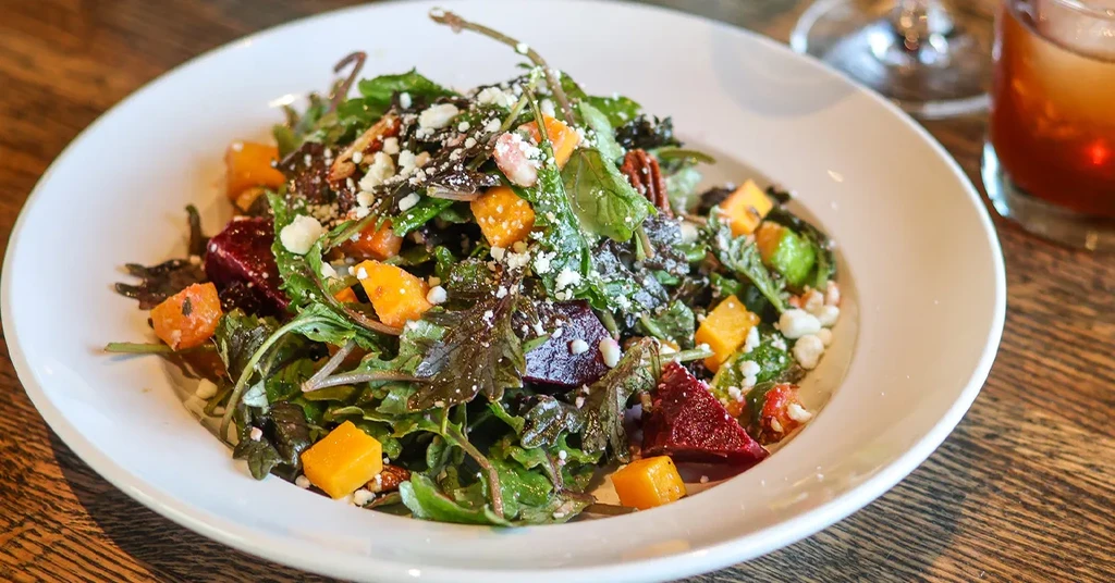 Colorful salad with greens, orange squash, beets, cheese, and pecans.