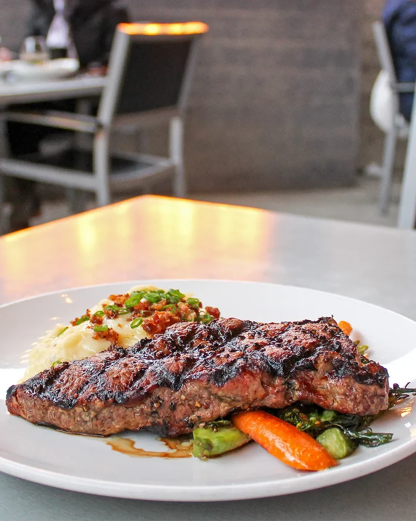 Grilled steak, mashed potatoes, vegetables on a plate with restaurant background.