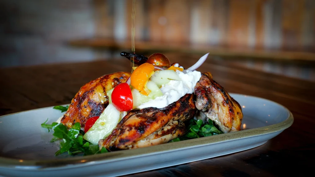 Grilled chicken, fresh salad, creamy sauce, and oil being poured.