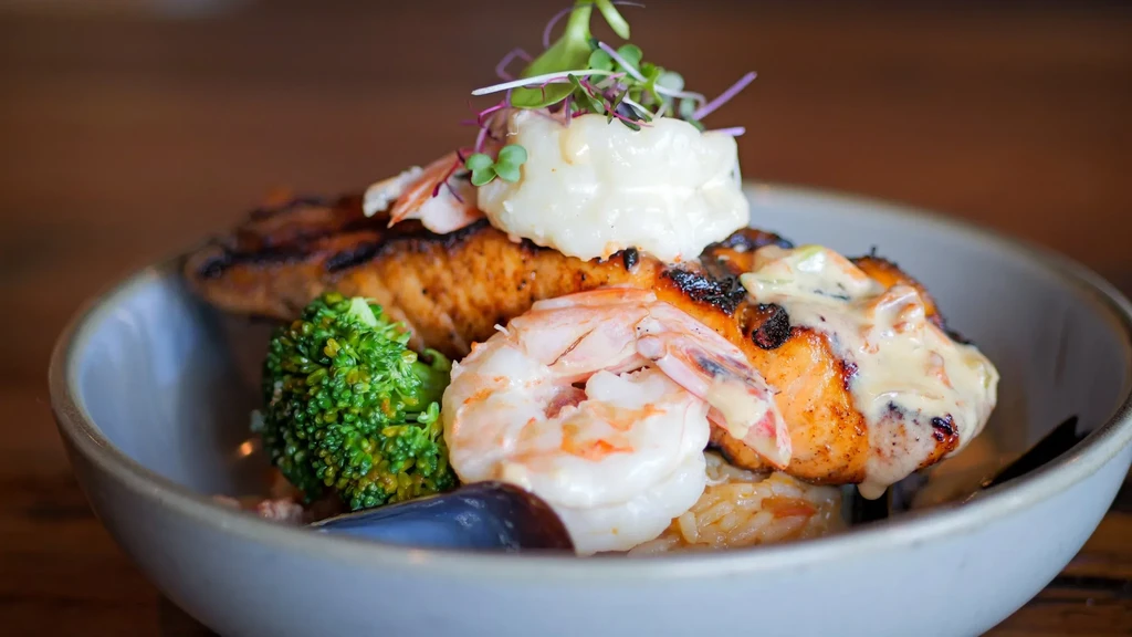 Grilled salmon, shrimp, scallop, broccoli, microgreens in a bowl.