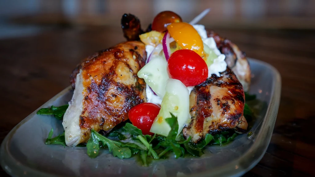 Grilled chicken pieces with tomato salad, greens, and creamy dressing.