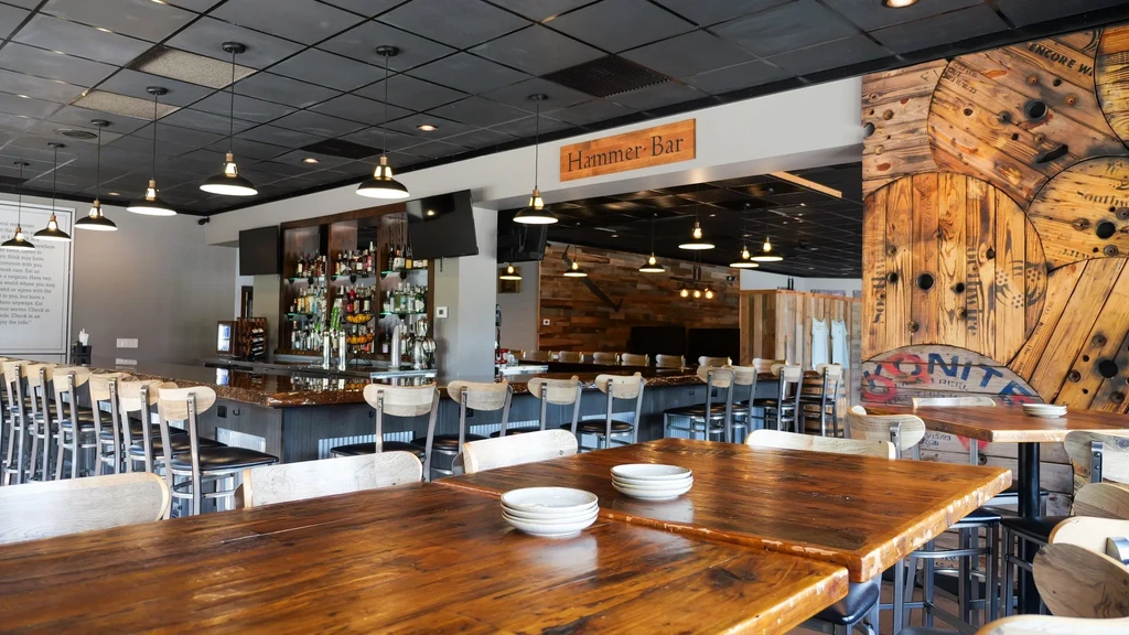 Empty, industrial-rustic Hammer-Bar interior with tables, long bar, pendant lights.