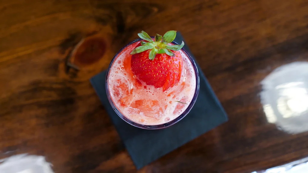 Top-down, frothy red drink with a whole strawberry in a glass.
