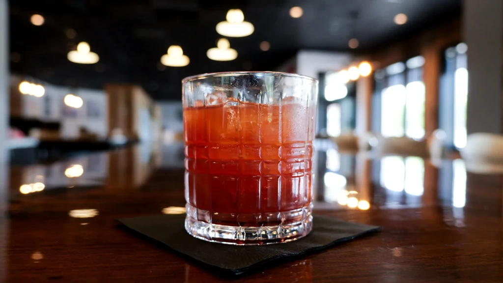 Red drink with ice in a textured glass, blurred bar background.