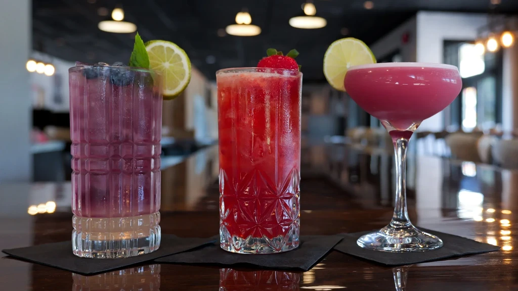 Three vibrant, garnished cocktails on a polished wooden surface.
