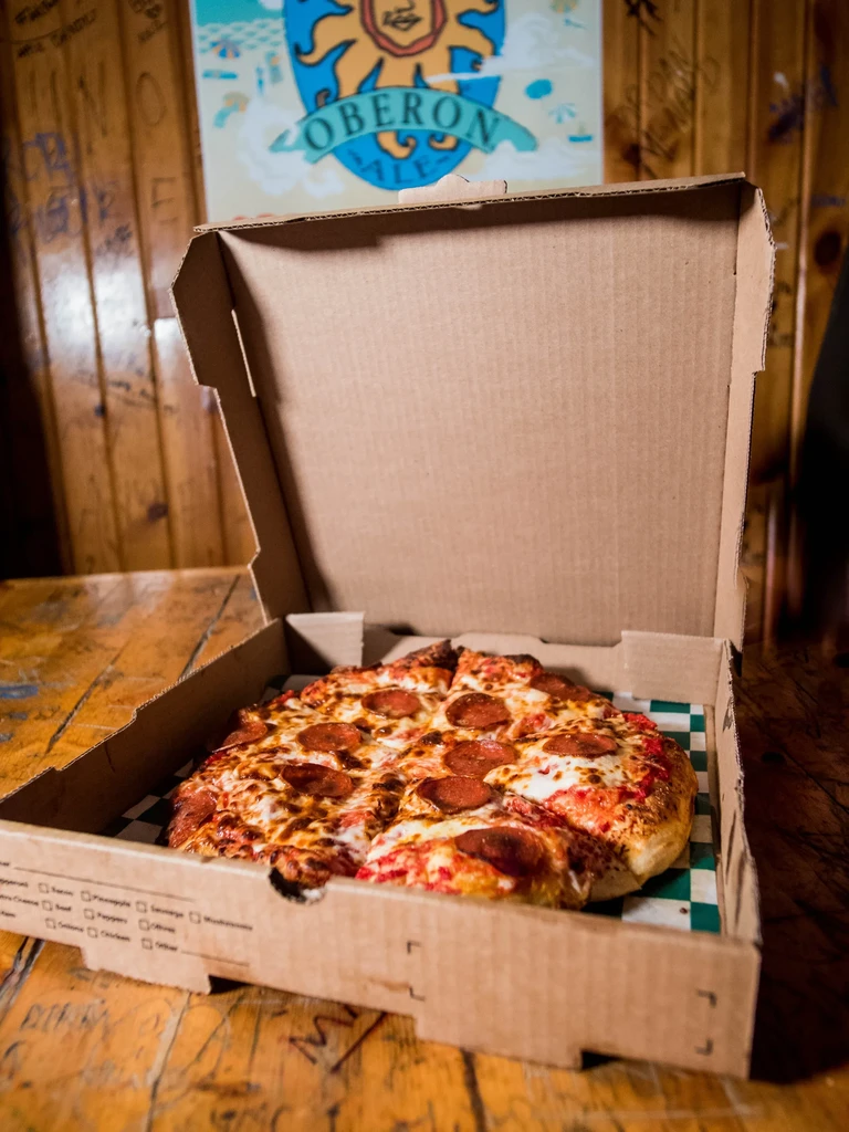 Sliced pepperoni pizza in an open box on a rustic wooden table.