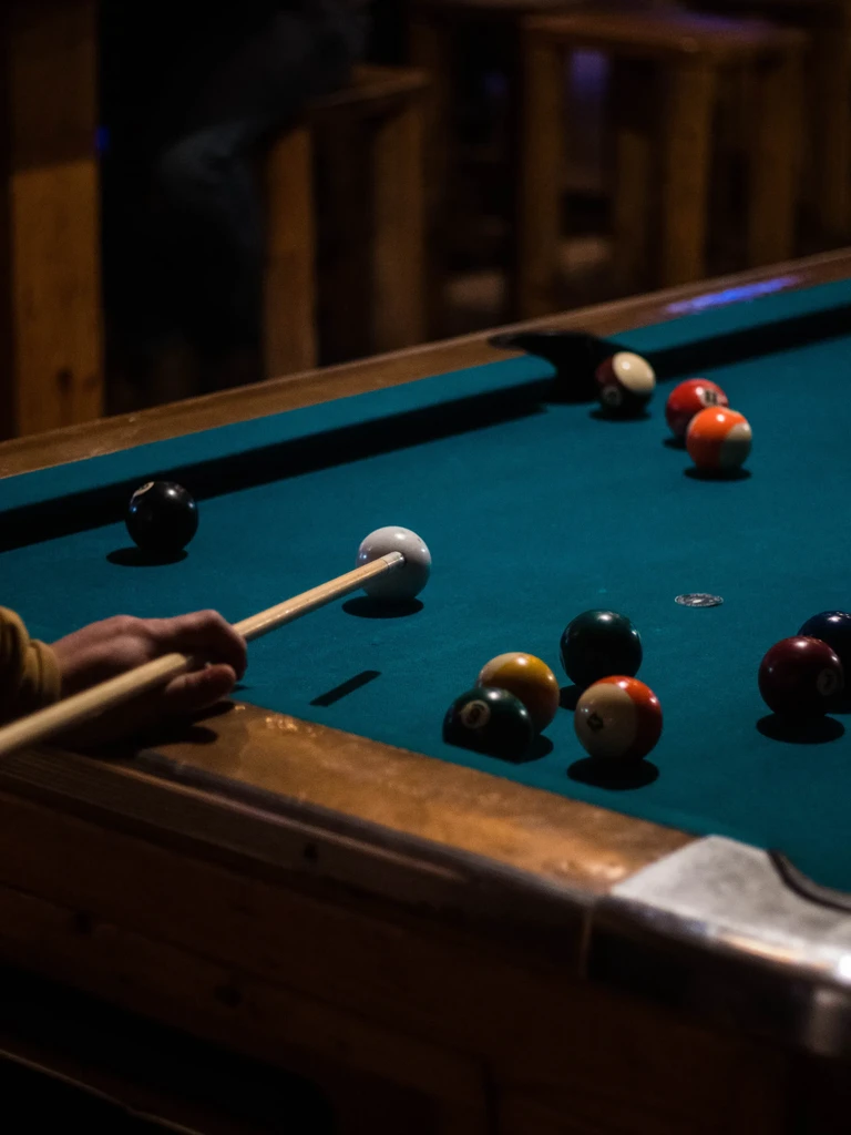 Hand holding cue stick over billiard balls on a teal pool table.