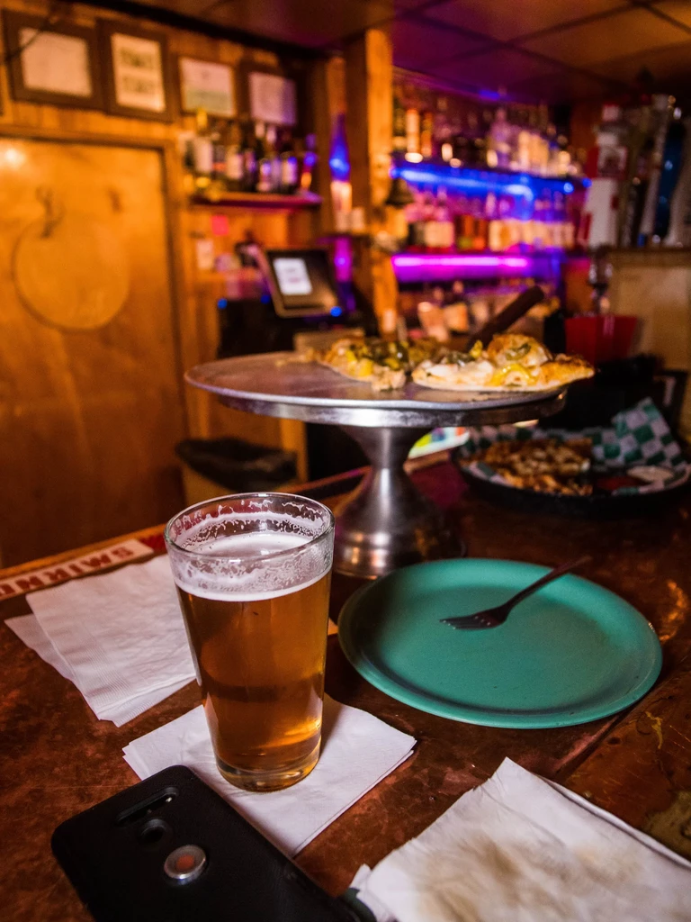 Beer, smartphone, and pizza slices on a bar with neon lights.