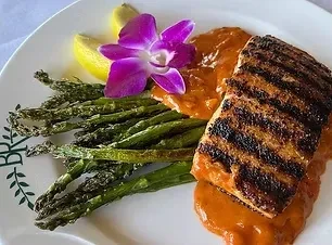 Grilled fish, asparagus, orange sauce, lemon, and orchid on white plate.