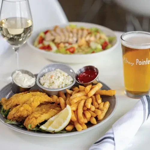 Fried fish and chips, condiments, wine, and beer on a table.