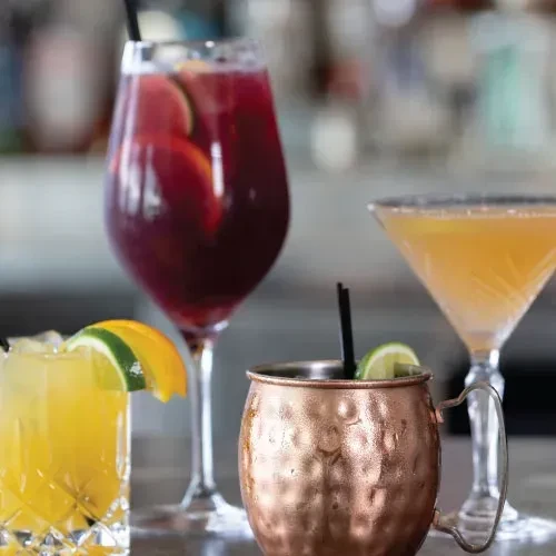 Four colorful cocktails in different glasses on a bar.