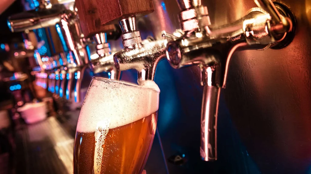 Golden amber beer with frothy head pours from tap into glass.