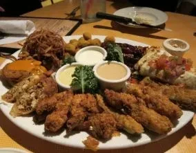 Platter of fried appetizers, shredded meat, dips, and bruschetta on a table.