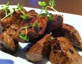 Close-up of seared meat pieces with green garnish on a white plate.