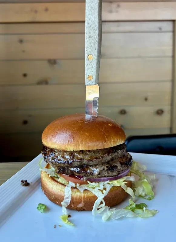 Double cheeseburger with a knife, brioche bun, cheese, tomato, lettuce.