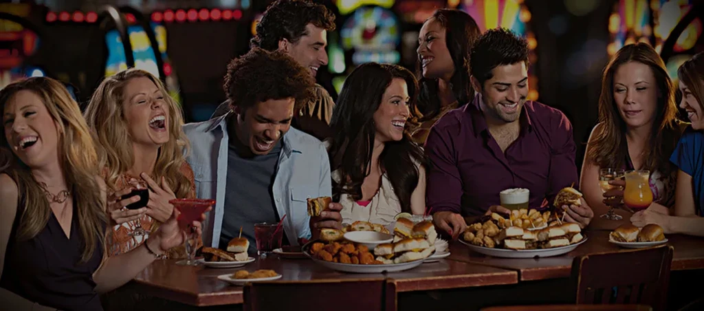 Eight diverse young adults smiling, eating and drinking together.