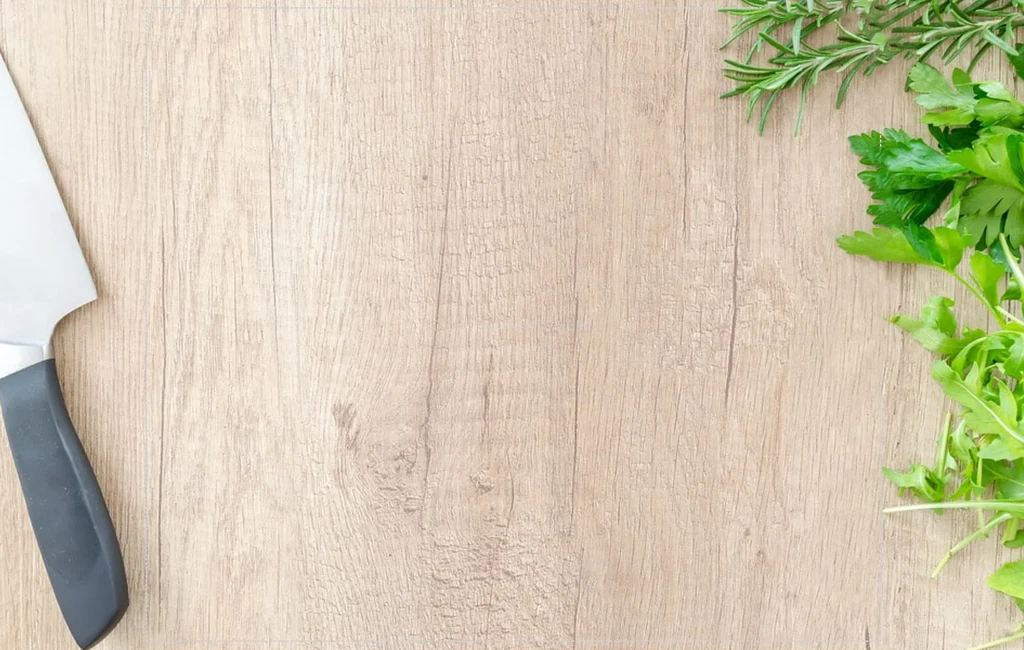 Fresh green herbs, chef's knife on a light wooden board.
