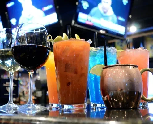 Vibrant drinks on a bar top, blurred TVs showing sports.