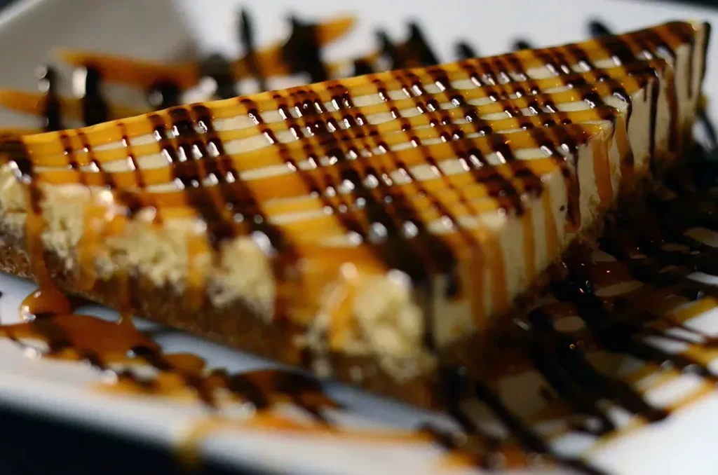 Cheesecake slice with caramel and dark sauce lattice.