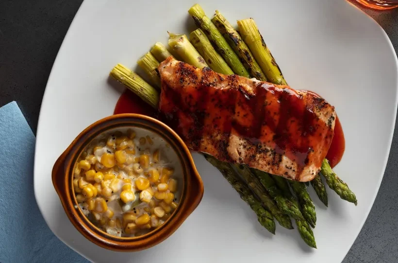 Grilled fish with dark sauce, green asparagus, and creamed corn.