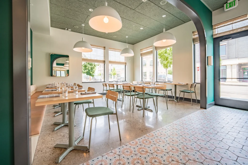 Bright, empty modern restaurant with green walls and light wood furniture.